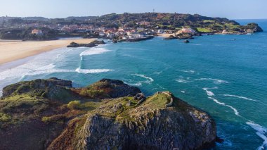 Kayalık bir ada, kumlu Cuarezo plajı, Atlantik Okyanusu 'nun mavi suları ve yeşil yamaçlara kurulmuş Isla köyü. Ada, Cantabria, İspanya.