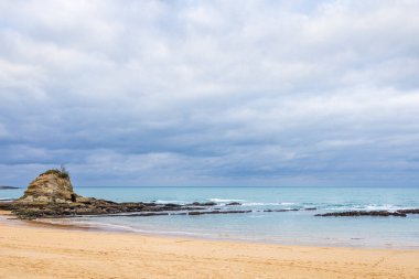 Kışın terk edilmiş bir Camel Sahili (Playa del Camello). Cantabrian Denizi 'nin masmavi suları, alçak kütleli bulutlar, kumlu bir plaj ve küçük dağlı kayalık bir bölge. Santander, Cantabria, İspanya.