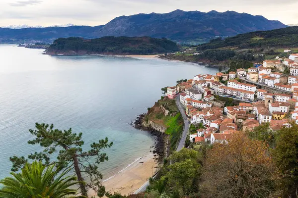 Lastres 'in panoramik hava manzarası, sahil, körfezin sakin suları ve Sierra del Sueve' in çevresindeki dağ zirveleri. San Roque bakış açısı. Lastres, Asturias, İspanya.