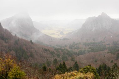 İki kayalık tepe, Tuiliere ve Sanadoire, Sancy-Monts Dore kompleksini oluşturan ve bir vadiyle ayrılan iki volkanın kalıntıları. Bulutlar ve sağanak yağmur. Orcival, Massif Central, Fransa.