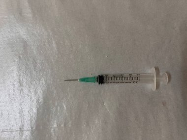 Gri zemin üzerinde beyaz bir sıvı bulunan şırınga, üst görünüm