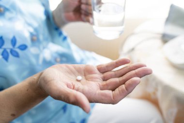 senior woman feeling sick, taking medicines in hand with a glass of water at home. Elderly and healthcare concept