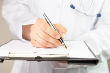 Tanımlanamayan bir doktorun modern bir hastanedeki bir dosyaya notlar yazarken görüntüsü.
