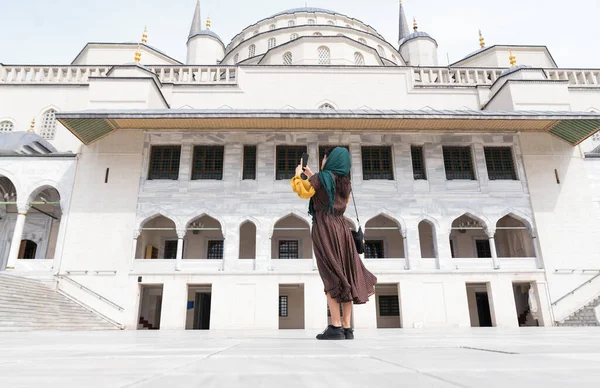 Orta Doğulu genç bir kadın telefonla fotoğraf çekiyor. Cami ceketli Müslüman kadın.