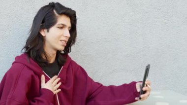 İkili olmayan kişi açık havada akıllı telefon kullanıyor. Video görüşmesi yapıyor.