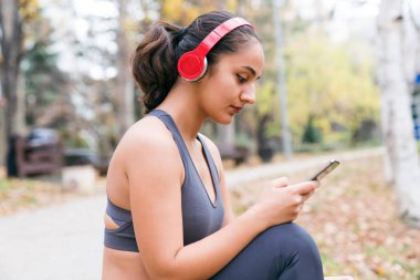Antrenmandan sonra akıllı telefon ve kulaklık kullanan bir kadın.