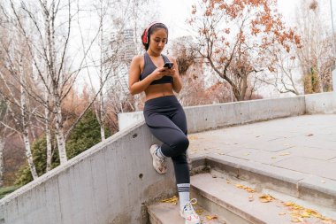 Antrenmandan sonra akıllı telefon ve kulaklık kullanan bir kadın.