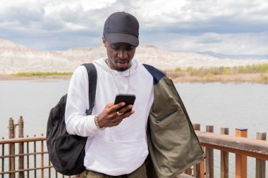 Yakışıklı genç zenci adam dışarıda cep telefonunu kullanıyor.