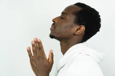 Genç siyah adam dua ediyor, beyaz arka planda izole edilmiş.