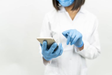 Elinde telefon olan tıbbi maskeli bir kadın doktor.