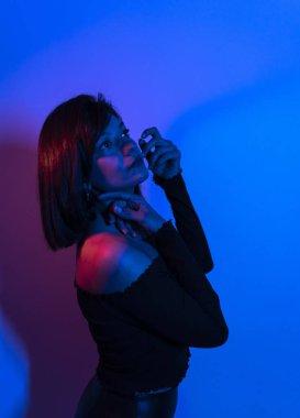 Renkli parlak neon ışıklarıyla stüdyoda poz veren yüksek model kadın. Parlak makyajlı güzel bir kadının portresi. Sanat tasarımı canlı biçimi