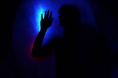 Mavi ışığın arkasındaki siluet kadın gizemli ve sanatsal bir şekilde poz veriyor.