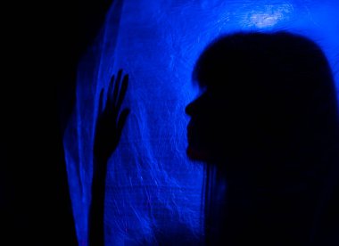 Mavi ışığın arkasındaki siluet kadın gizemli ve sanatsal bir şekilde poz veriyor.