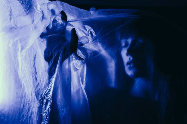 Mavi ışığın arkasındaki siluet kadın gizemli ve sanatsal bir şekilde poz veriyor.