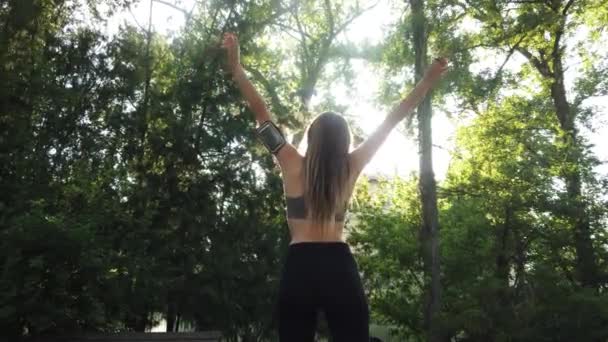公園の屋外で走る前に伸びる若い女性 日光は木を通って輝く — ストック動画