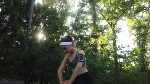 公園の屋外で走る前に伸びる若い女性 日光は木を通って輝く — ストック動画