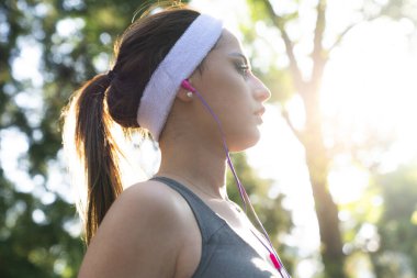 Parkta koşan genç fitness sporcusu kadın. Sabahları doğada koşarken kulaklıkla müzik dinleyen mutlu atletik kadın..