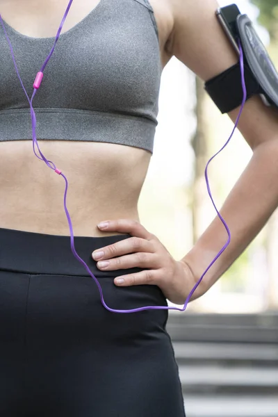 Spor kıyafeti giyen bayan sporcu ve müzik dinlemek için akıllı telefon kullanıyor.