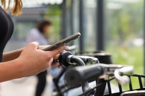 young woman holding smartphone using bike rental digital phone app scanning qr code to rent electric bicycle in city