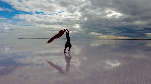 一个美丽的女人带着丝巾优雅地在海边跳舞 她的动作流畅而轻松 体现了欢乐与自由的本质 — 图库视频影像