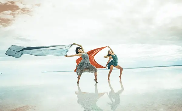 two women gracefully dances on the beach by the sea on a summer day