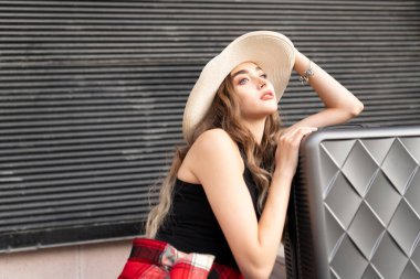 Güzel bir kız hasır şapkayla parkta bavulla poz veriyor.