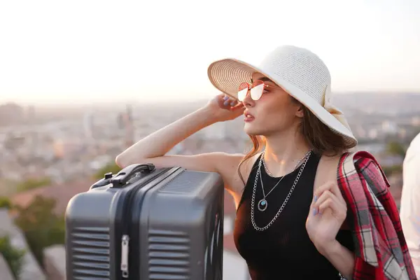 Gün batımında şapkalı ve güneş gözlüklü genç bir kadın.