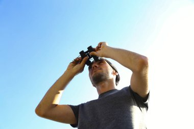 Gökyüzünün arka planında dürbünlü bir adam