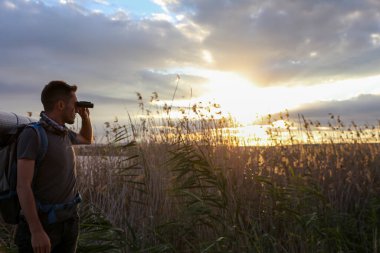 Günbatımında sırt çantalı ve dürbünlü erkek turist