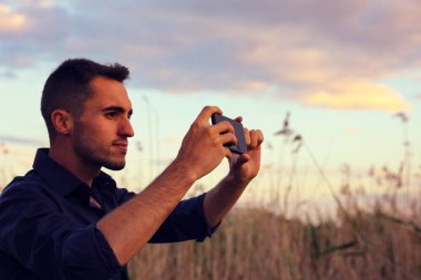 Kameralı genç adam gün batımında sahada fotoğraf çekiyor.. 