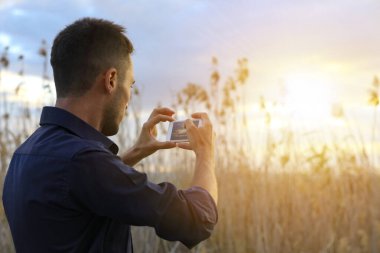 Adam fotoğrafçı akıllı telefonuyla gün batımının fotoğrafını çekiyor.