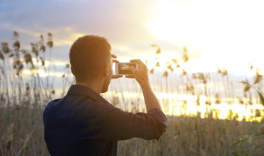 Adam fotoğrafçı akıllı telefonuyla gün batımının fotoğrafını çekiyor.