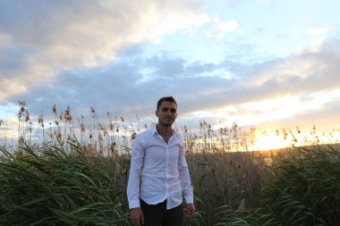 Beyaz gömlekli bir adam gün batımında kırsalda yürüyor.