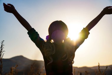 Ekose gömlekli sarışın bir kadın uzun otların arasında duruyor. Mutlu kadın yaz günü gün batımında dışarıda doğanın tadını çıkarıyor.