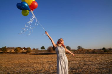 Yazın gün batımında balonlu genç ve mutlu bir kadın. Mutlu kadın koşuyor ve gün batımında balonlarla eğleniyor.