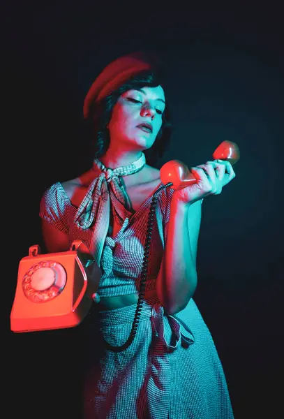 Young Woman Talking on Orange Retro Phone. High Fashion model woman in colorful bright neon blue and purple lights posing in studio.