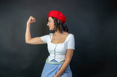 Kırmızı şapkalı ve beyaz gömlekli bir kadın kolunu esnetiyor. Görüntünün güçlü, kendinden emin bir havası var.