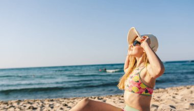 Kumsalda güneşlenen, güneşin ve tatilin tadını çıkaran güzel genç bir kadın.