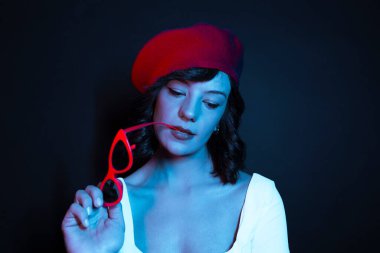 Kırmızı şapkalı ve kırmızı gözlüklü bir kadın stüdyoda poz veriyor. Renkli arka planda zarif bir kadının portresi