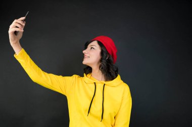 Sarı kazak giyen mutlu genç bir kadın cep telefonuyla selfie çekiyor.