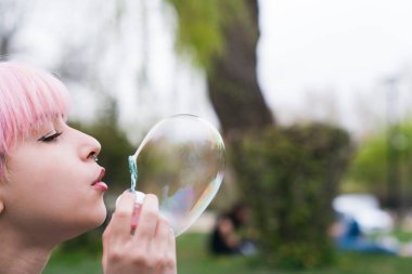 Dışarıda sabun köpüğü üfleyen mutlu, genç bir kadın.
