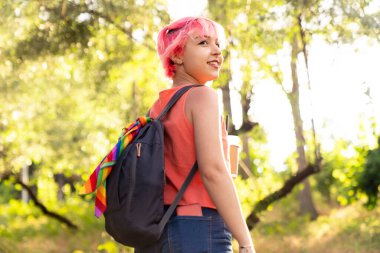 Pembe saçlı genç bir turist kız sırt çantasına bakıyor ve doğada geziyor.