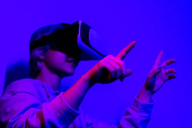 Mor saçlı bir kadın VR kulaklık takıyor ve ekrana bakıyor.