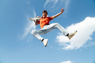 Kolları açık bir adam havaya zıplıyor. Gökyüzü mavi ve arka planda bulutlar var. Manzara neşeli ve enerjik.