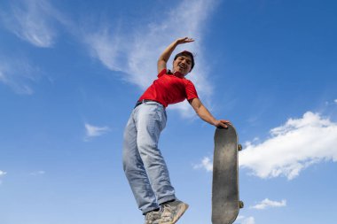 Genç adam arka planda mavi ve bulutlu bir kaykayla mutlu poz veriyor. gençlik sporları ve eğlence konsepti