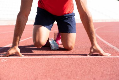 Koşucunun yakın çekimi başlangıç çizgisinde çalışmaya hazır. Yarışa başlamak için başlangıç çizgisinde bekleyen bir erkek sporcunun fotoğrafı.