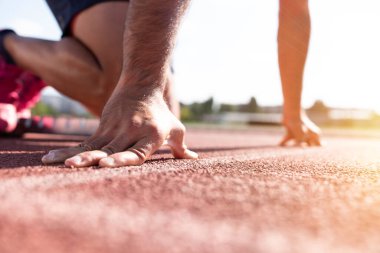 Koşucunun yakın çekimi başlangıç çizgisinde çalışmaya hazır. Yarışa başlamak için başlangıç çizgisinde bekleyen bir erkek sporcunun fotoğrafı.