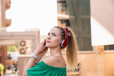 Şehirde kulaklık takan ve gülümseyen mutlu bir kadın. Kulaklıkla müzik dinlemek.