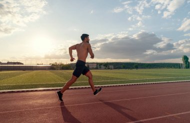 Arka planda bulutlu bir gökyüzü olan bir adam yolda koşuyor.