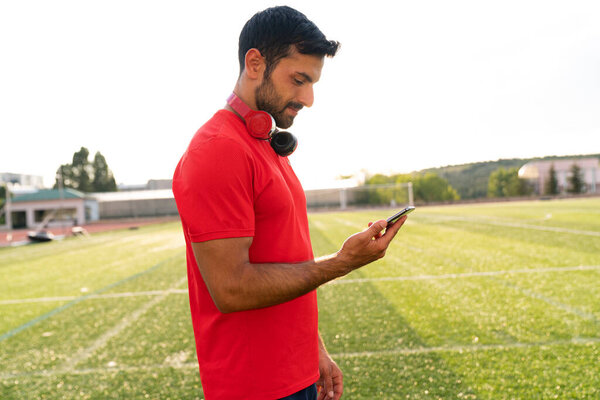 человек, использующий смартфон в городском парке после тренировки на открытом воздухе. Спортсмен после тренировки пишет смс-ки на экран телефона..